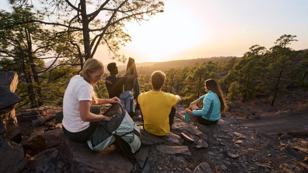 Vier Menschen ruhen sich auf Felsen in einer natürlichen Umgebung bei Sonnenuntergang aus.