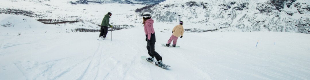 Twee snowboarders en een skiër dalen een besneeuwde berg af.