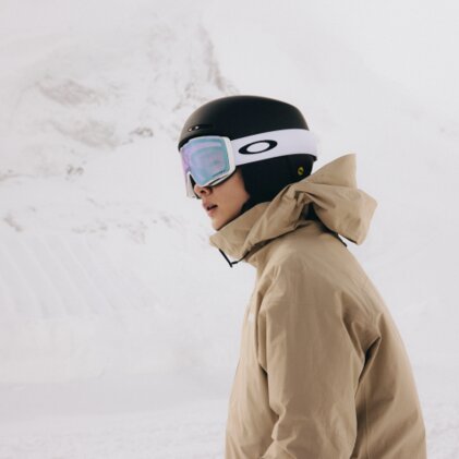 A person wearing snowboarding gear, including a helmet, jacket, and ski goggles, is ready to go snowboarding in the snow.
