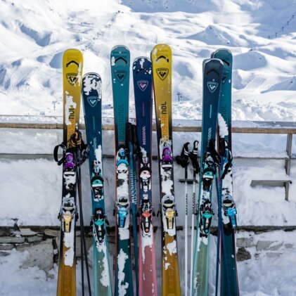 Mehrere bunte Rossignol-Skis und Skistöcke stehen aufrecht im Schnee vor einer verschneiten Berglandschaft und klarem blauen Himmel. | © INTERSPORT International Corporation GmbH