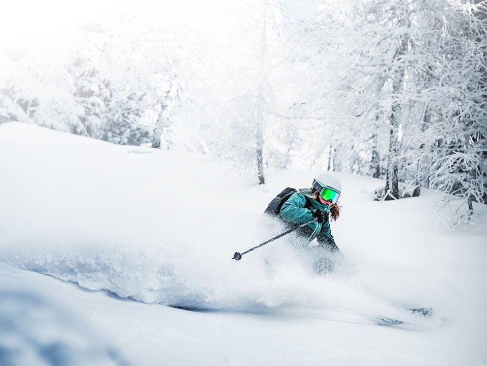 Skier carving through deep powder in a snowy forest. | © Atomic Austria GmbH