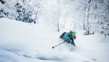 Skifahrerin im Tiefschnee zwischen verschneiten Bäumen | © Atomic Austria GmbH