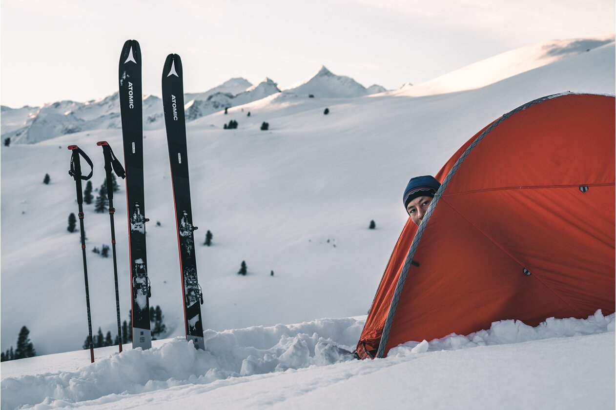 Person peeking out of an orange tent in a snowy mountain landscape. | © Atomic Austria GmbH
