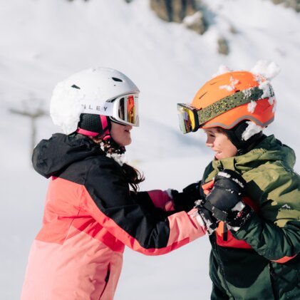 Deux enfants en équipement de ski et casques se regardant sur les pistes.