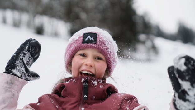 Fillette souriante dans la neige avec bonnet et gants. | © INTERSPORT International Corporation GmbH