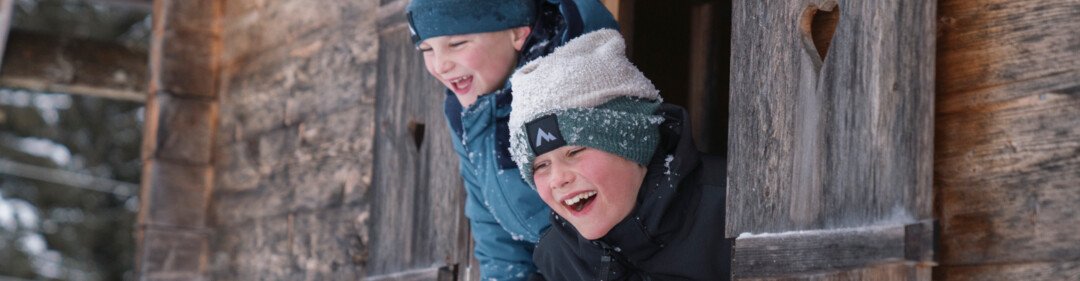 © INTERSPORT International Corporation GmbH Twee lachende jongens kijken uit een raam met een hartvormige uitsparing. | © INTERSPORT International Corporation GmbH