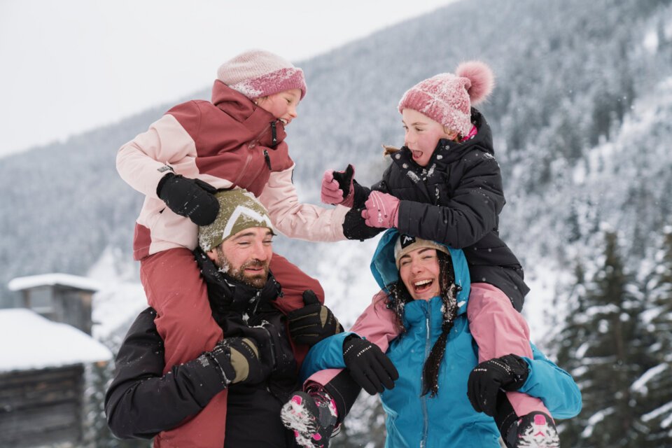 Eine Familie hat Spaß im Schnee, wobei die Eltern ihre Kinder Huckepack nehmen. | © INTERSPORT International Corporation GmbH