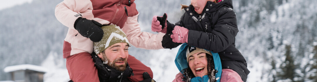 Een gezin heeft plezier in de sneeuw, waarbij de ouders hun kinderen een lift geven op hun rug. | © INTERSPORT International Corporation GmbH