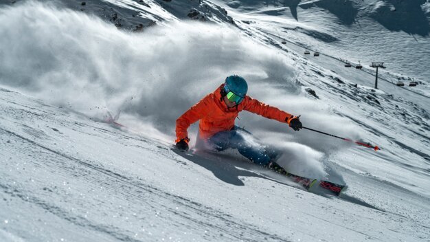 Skieur en veste orange dévalant une pente enneigée. | © Fischer Sports GmbH