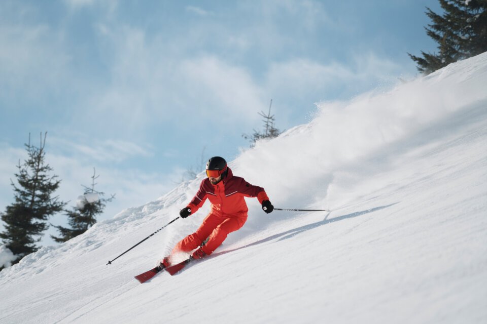 Skifahrer in rotem Anzug fährt einen schneebedeckten Hang hinunter. | © INTERSPORT International Corporation GmbH