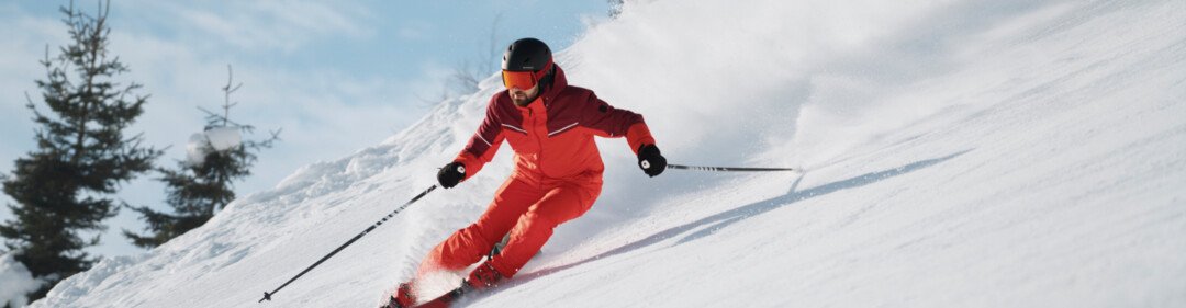 Skiër in rood pak skiet een besneeuwde helling af. | © INTERSPORT International Corporation GmbH