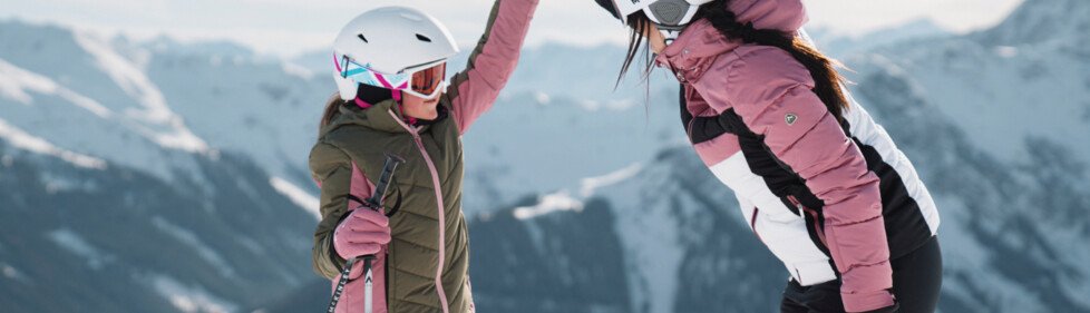 © INTERSPORT International Corporation GmbH Twee vrouwelijke skiërs geven elkaar een high-five voor een bergketen. | © INTERSPORT International Corporation GmbH