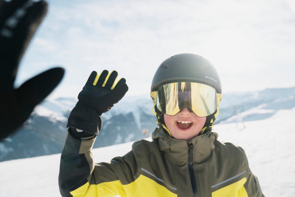 Boy in ski goggles and helmet waving on a ski slope. | © INTERSPORT International Corporation GmbH
