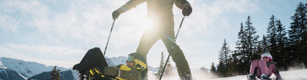 Skiër valt en wordt over skied, met een kind dat op de achtergrond zit. | © INTERSPORT International Corporation GmbH