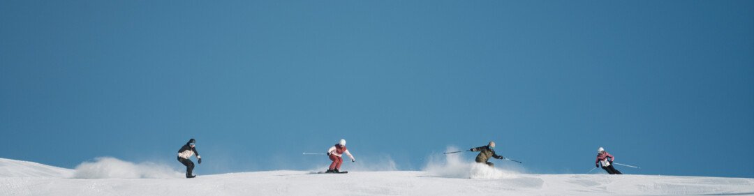 © INTERSPORT International Corporation GmbH Groep skiërs op een besneeuwde helling onder een blauwe lucht. | © INTERSPORT International Corporation GmbH
