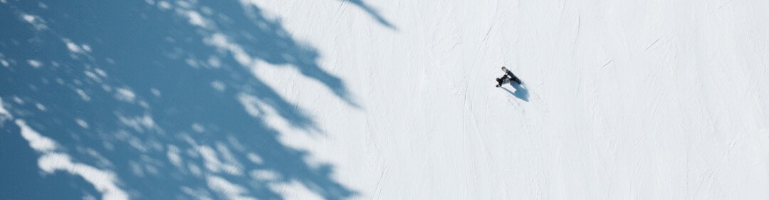 Luchtfoto van skiërs en snowboarder op een besneeuwde helling met boom schaduwen. | © INTERSPORT International Corporation GmbH