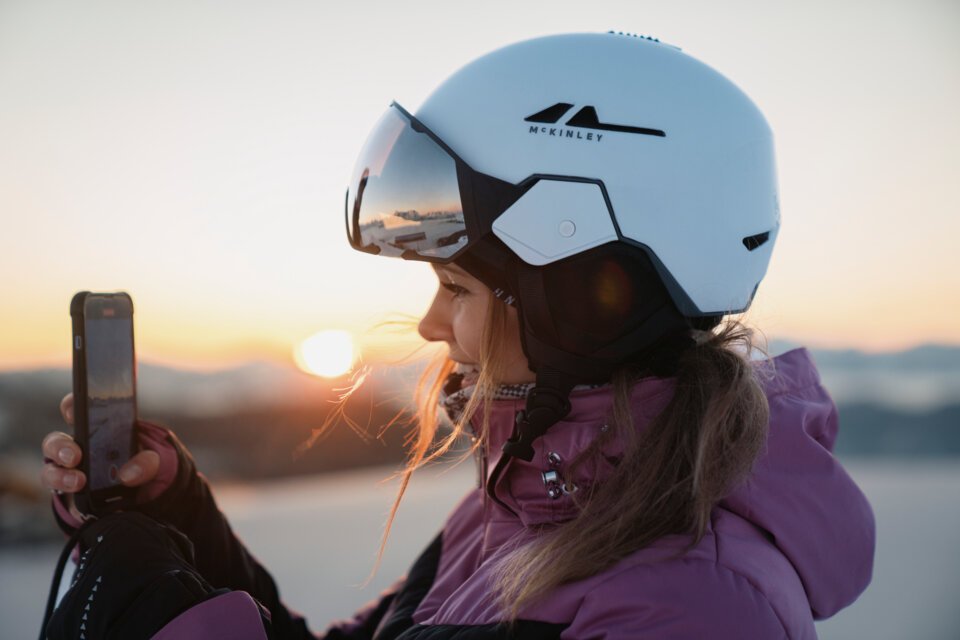 Femme avec casque de ski filmant le lever du soleil avec son téléphone | © INTERSPORT International Corporation GmbH