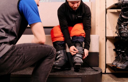 Homme attachant une chaussure de ski avec l'aide d'un vendeur.