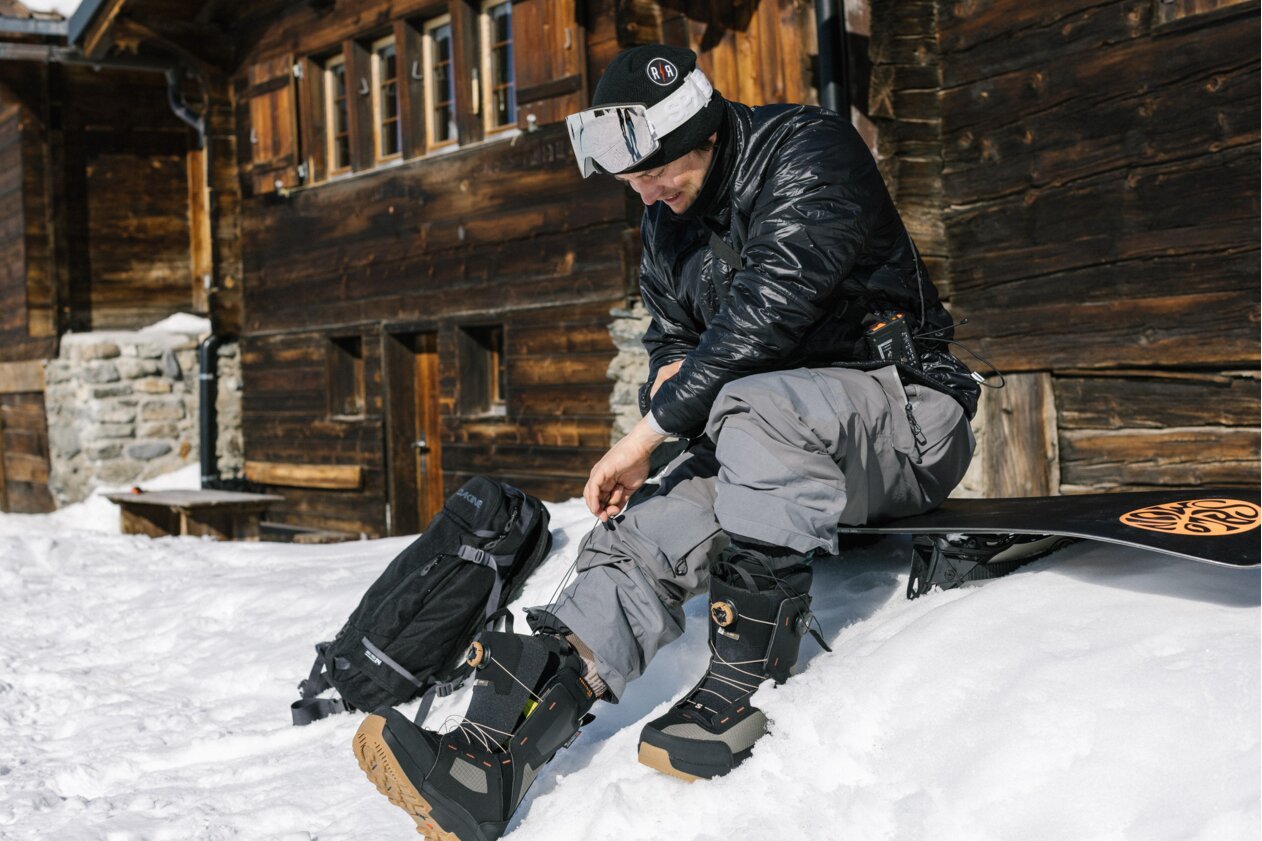 Snowboarder sitting and tightening his snowboard boots. | © Salomon