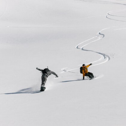 Twee snowboarders die een besneeuwde helling afdalen. | © Salomon