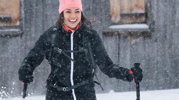 Frau beim Schneeschuhwandern im Schneefall lächelnd. | © IIC/McKINLEY