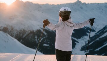 Skifahrerin genießt die Aussicht auf die schneebedeckten Berge bei Sonnenuntergang.