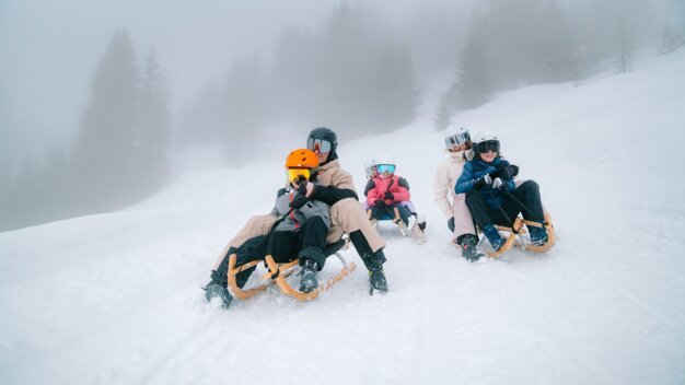 Familie rodelt auf einem schneebedeckten Hügel.