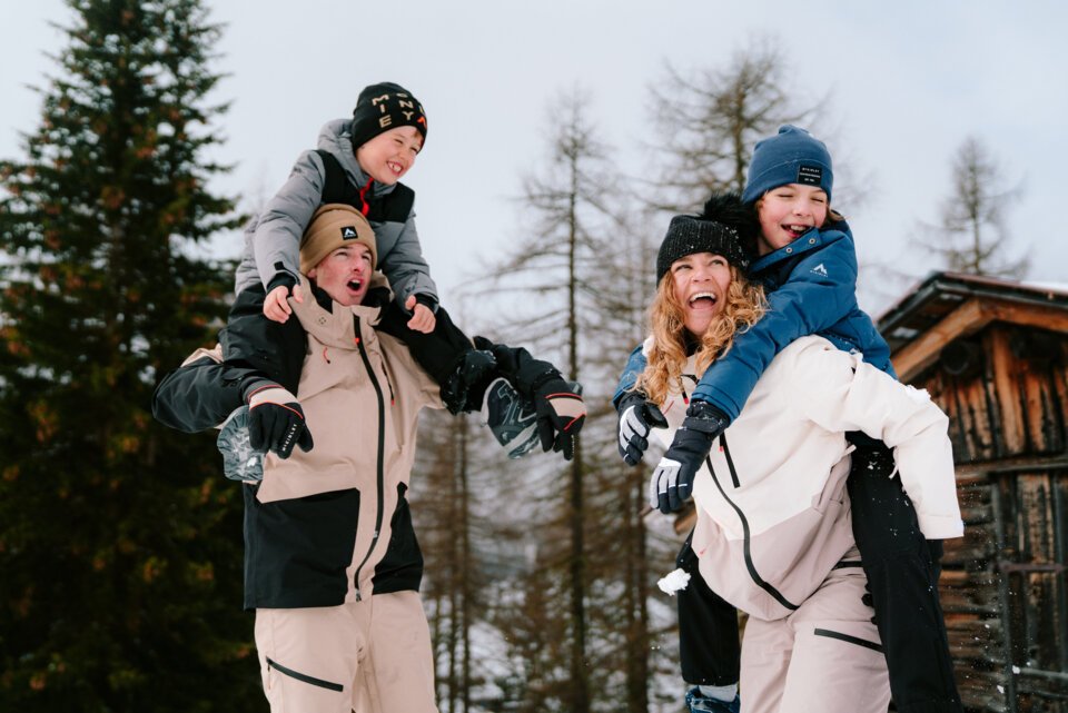 Father and mother giving their children piggyback rides in the snow.