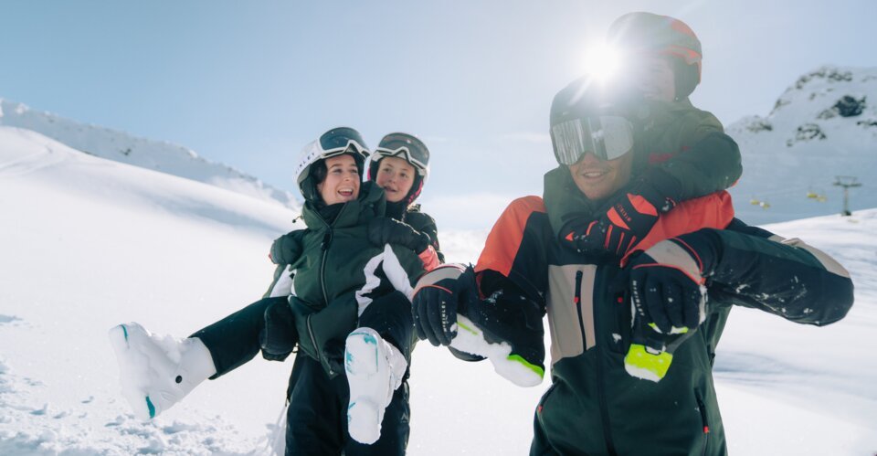 Vader draagt twee kinderen op zijn schouders in de sneeuw.