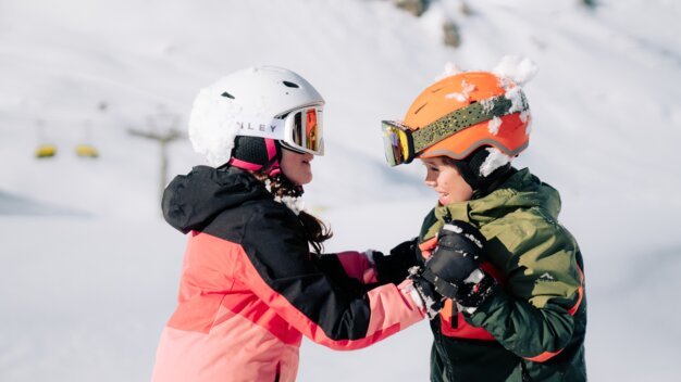Zwei Kinder in Skikleidung stehen im Schnee.