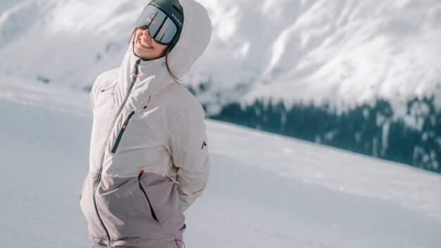 Frau mit Snowboardausrüstung kniet im Schnee vor Bergkulisse