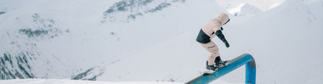 Snowboarder sur un rail bleu avec des montagnes en arrière-plan.
