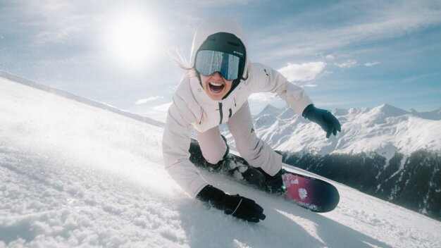 Femme faisant du snowboard sur une piste et souriant.