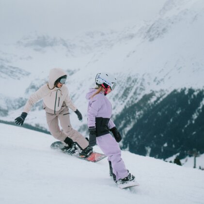 Deux snowboardeuses dévalent une pente enneigée.