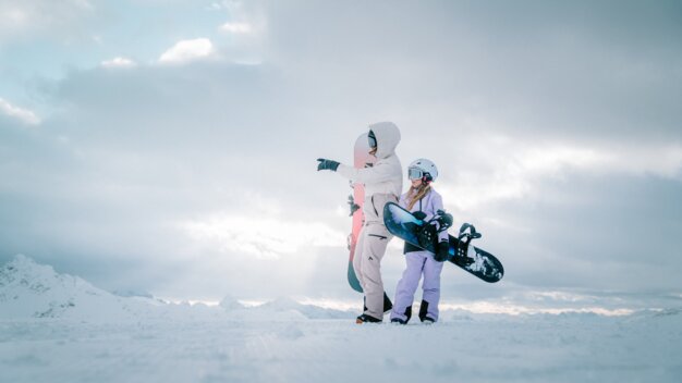 Zwei Snowboarderinnen stehen auf einem schneebedeckten Berg.