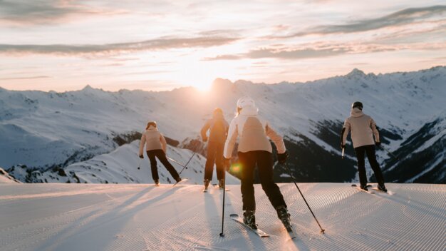 Groupe de skieurs dévalant une montagne au coucher du soleil.
