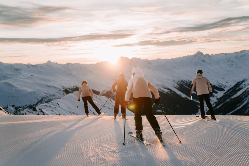Groep skiërs die een berg afskiën bij zonsondergang.