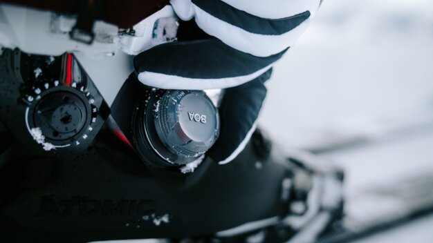 Gros plan d'une chaussure de ski avec une fermeture BOA et une main gantée rayée