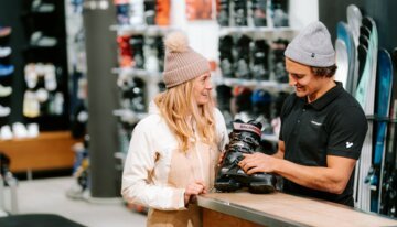 Une femme regarde avec approbation un vendeur qui lui montre des chaussures de ski.