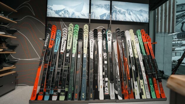 Rangée de skis de différentes marques et modèles dans un magasin.