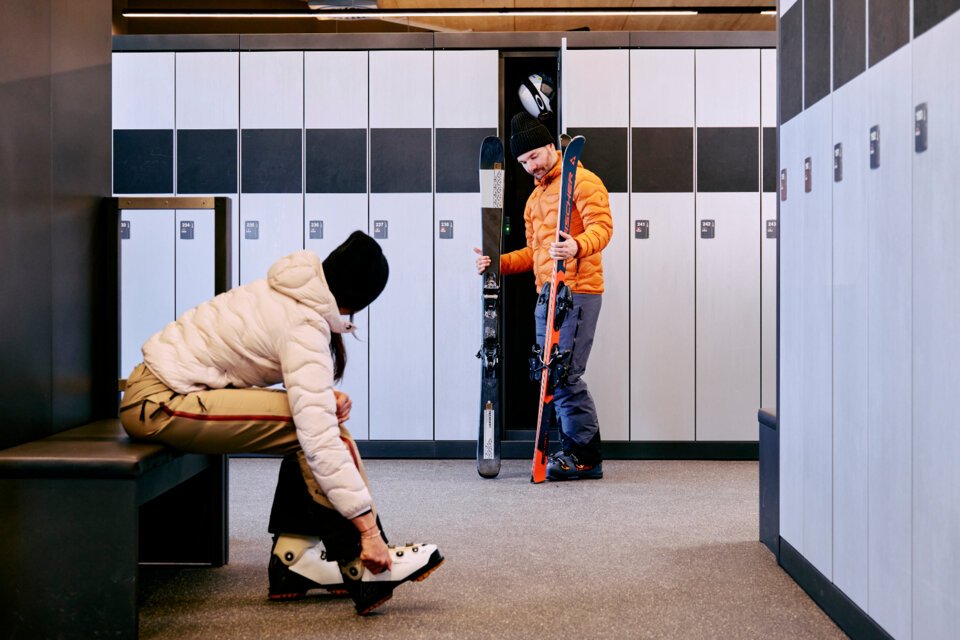 © ARMIN WALCHER Two people preparing to ski in a ski room. | © ARMIN WALCHER