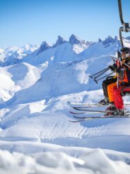 Skiers on a chairlift with snow-covered mountains in the background | © Cyrille Quintard / Alpe d’Huez Tourisme