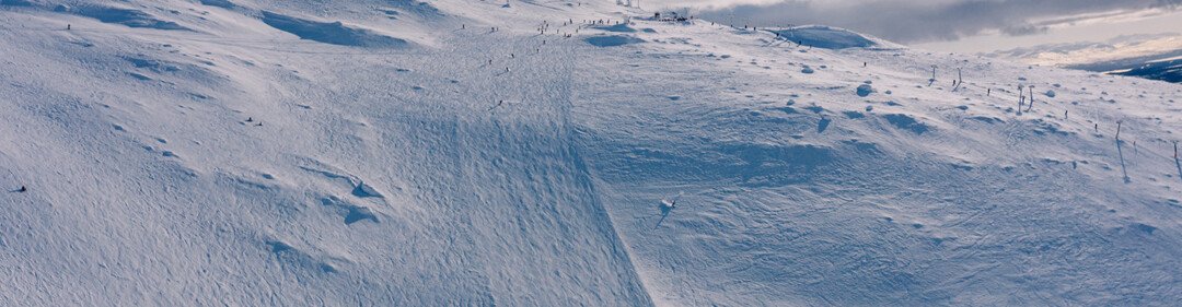 Besneeuwde skipiste onder een blauwe hemel met wolken.