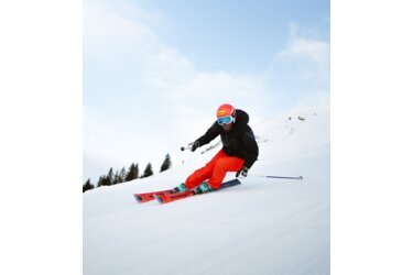 Skier in red pants and black jacket on a ski slope.